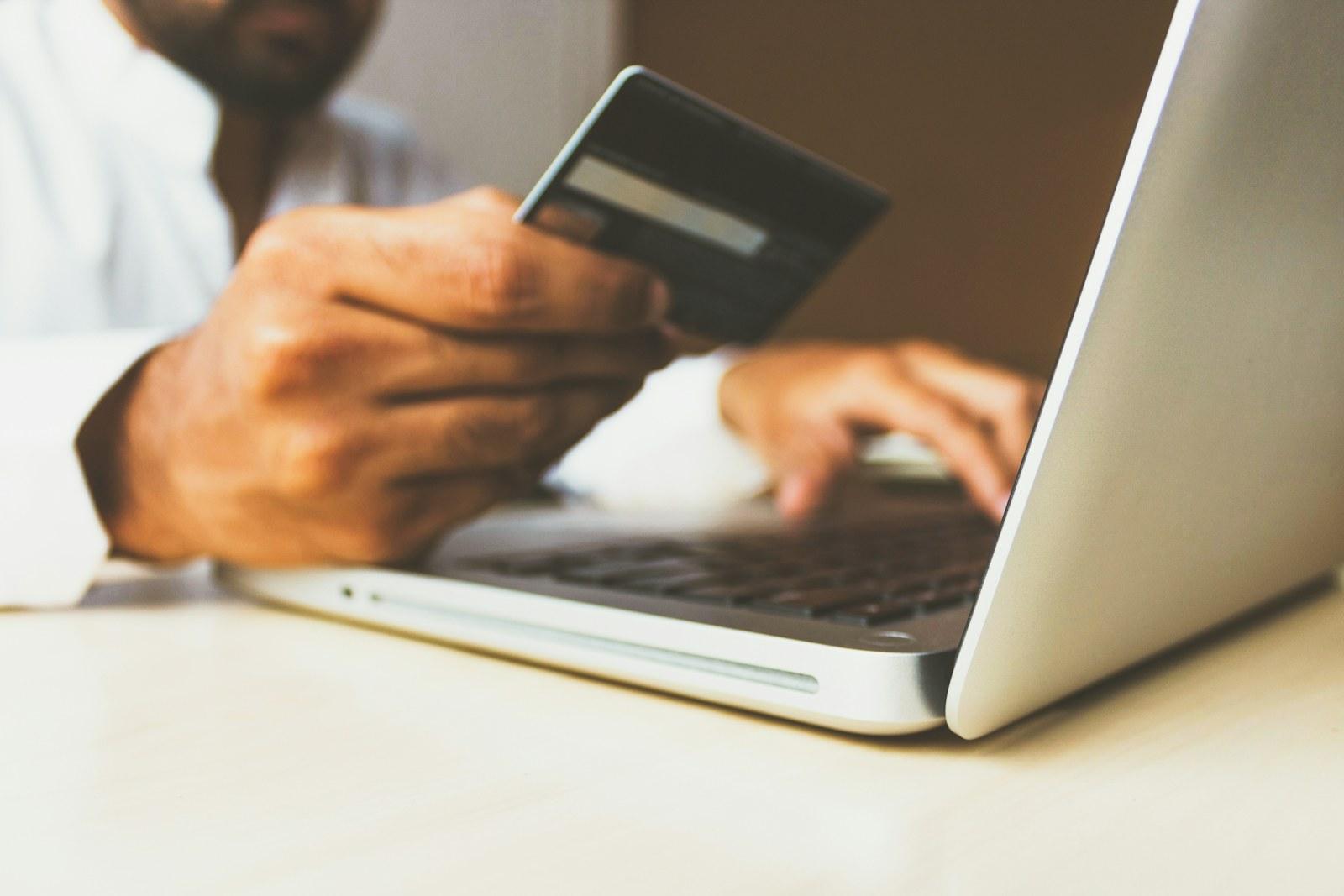 Person using a payment card beside a laptop