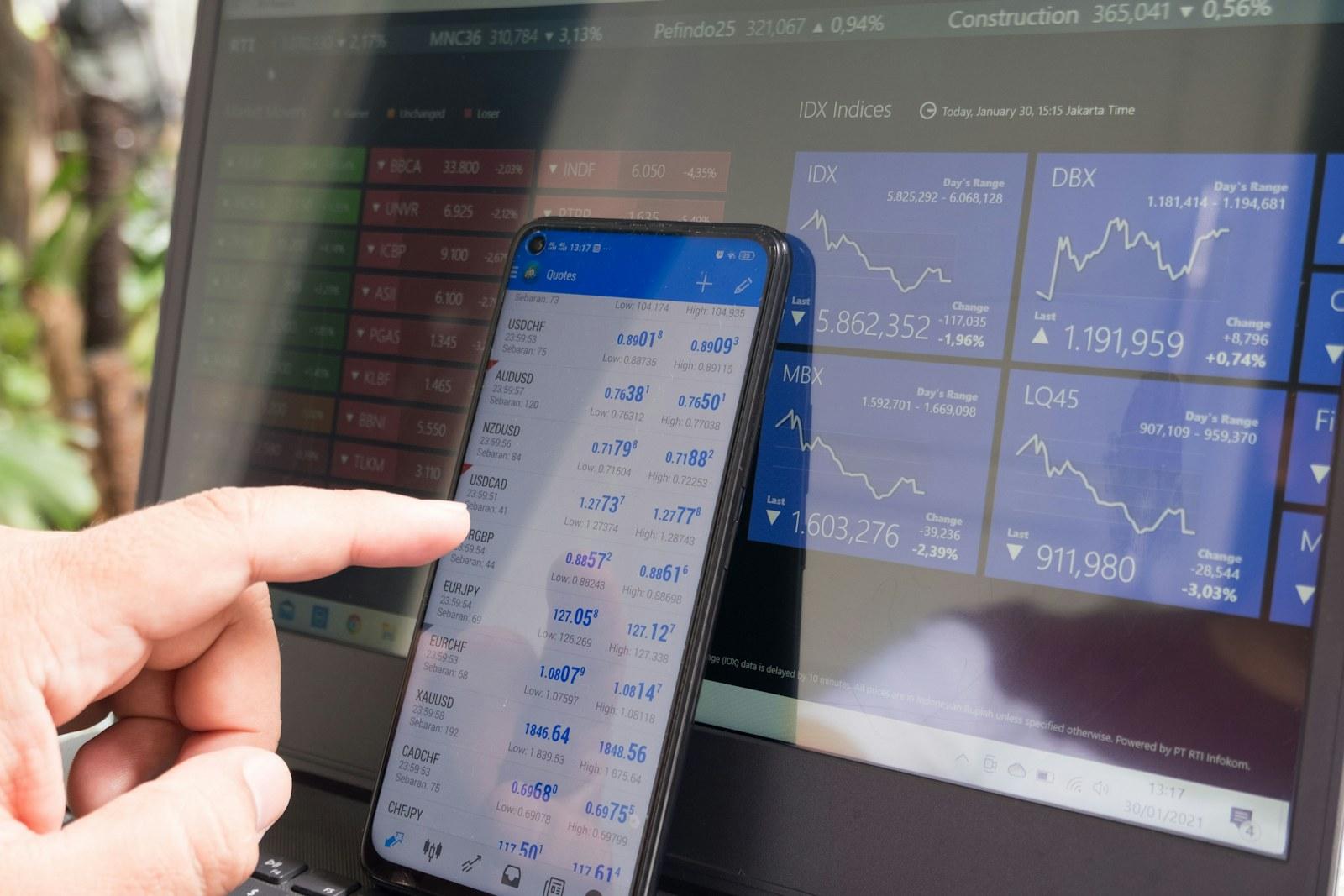 Person using a financial app on a phone beside a laptop